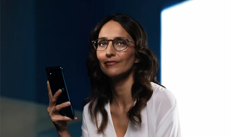 Essilor Varilux Physio extensee Transitions Gen S Lenses, official Essilor Varilux Physio extensee image of a woman in spectacles holding a smartphone