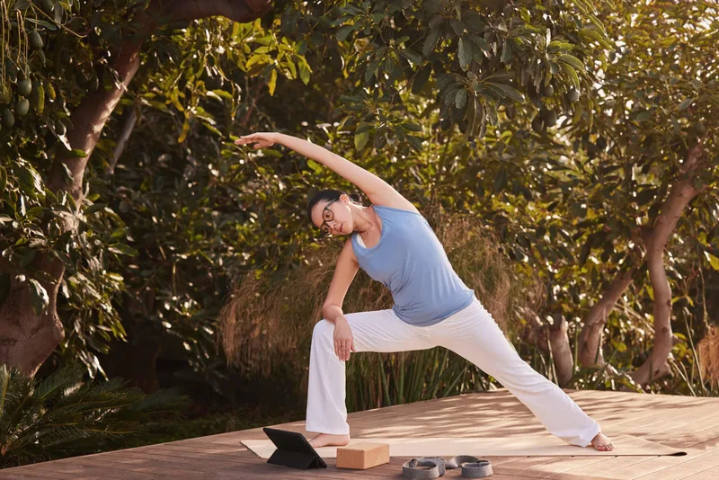 Essilor Varilux Comfort Max Transitions Gen S Lenses, Essilor Varilux Comfort Max photo of a woman in glasses doing a yoga stretch outdoors